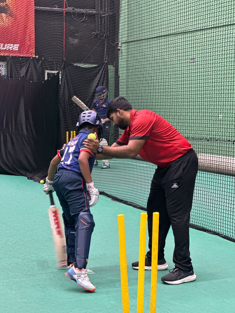 SPSA coach correcting a young batter's stance in the indoor nets at Dubai Investments Park