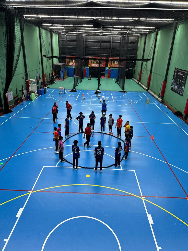 Kids warming up in a circle in the SPSA indoor cricket facility at Dubai Investments Park