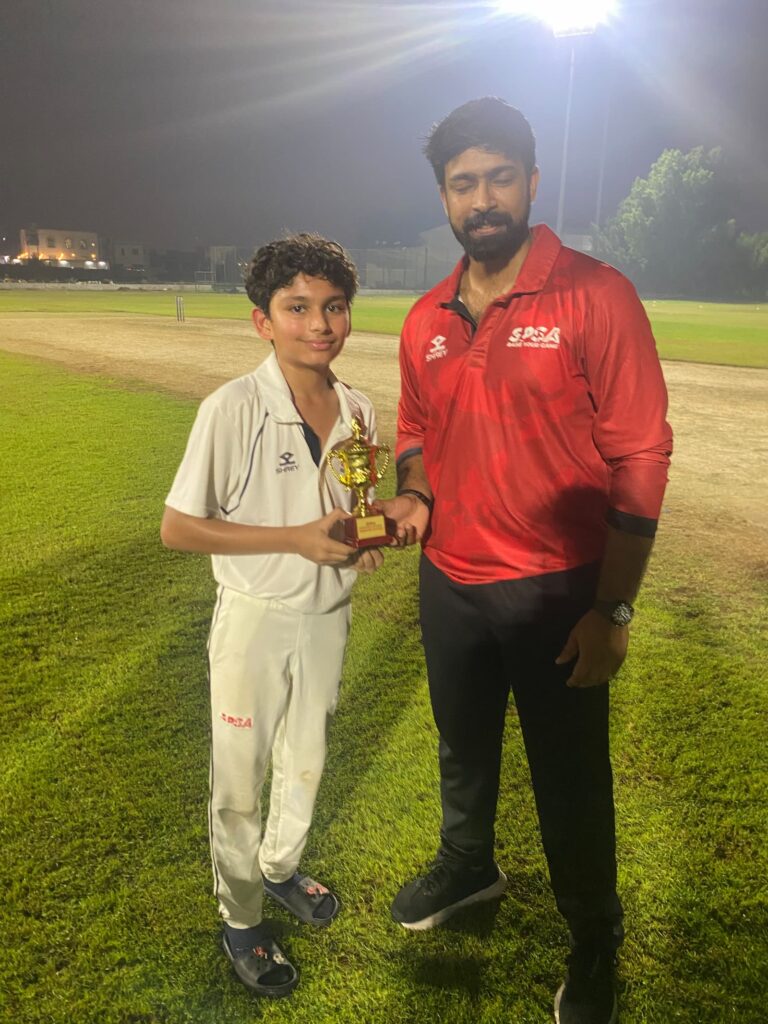 SPSA player receiving the best batter award from his coach under floodlights